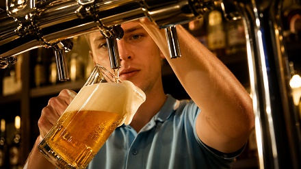 cerveza-tirada-sirviendo-bar-profesional Hombre profesional sirviendo cerveza tirada en jarra de vidrio, con espuma cremosa y abundante en bar equipado.